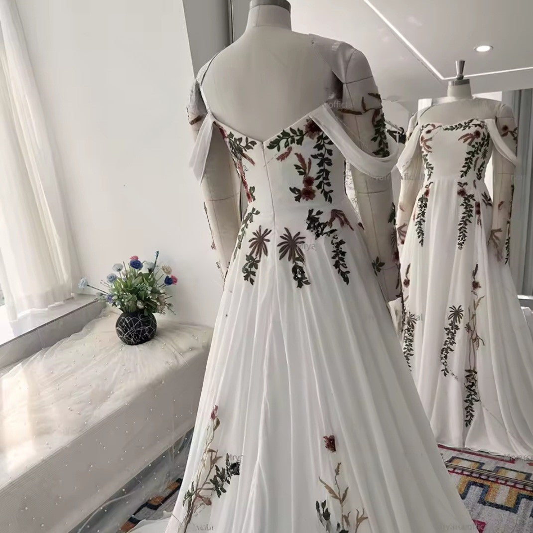 White dress with floral embroidery on a mannequin in a room with a window and flowers.