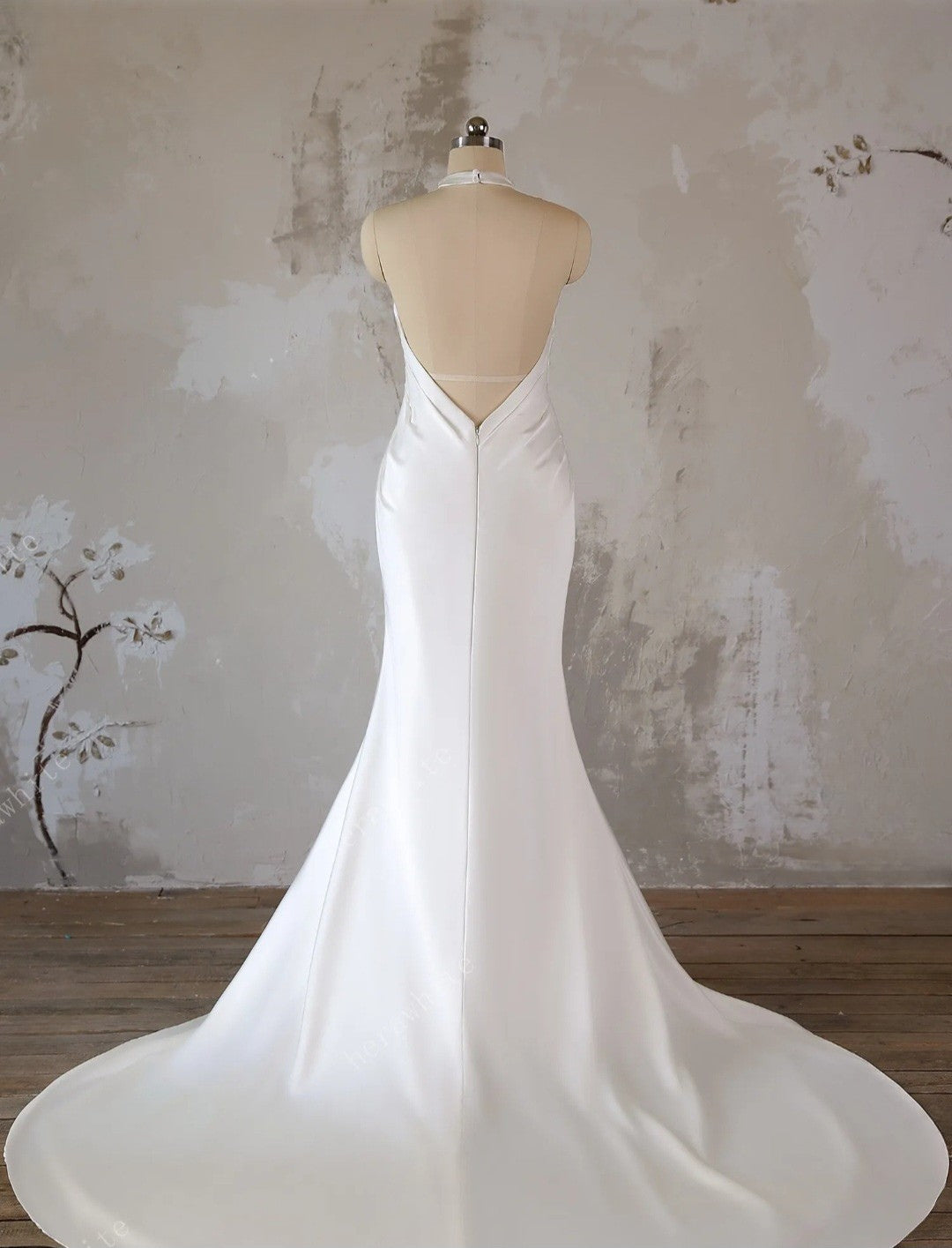 White wedding dress on a mannequin against a textured wall.