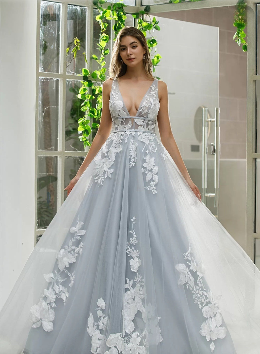 Woman wearing a light blue wedding dress with floral details in a bathroom setting.