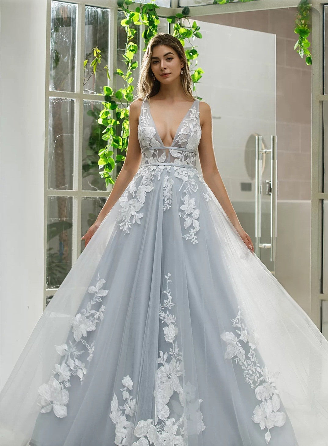 Woman wearing a light blue wedding dress with floral details in a bathroom setting.