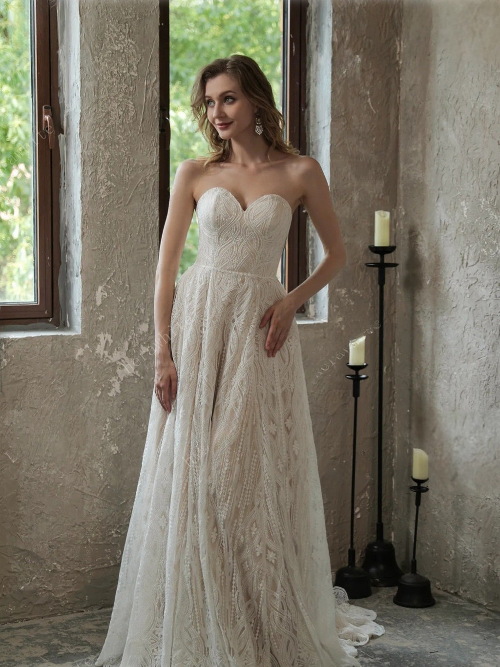 Woman in a strapless lace wedding dress standing in a rustic room with candles.