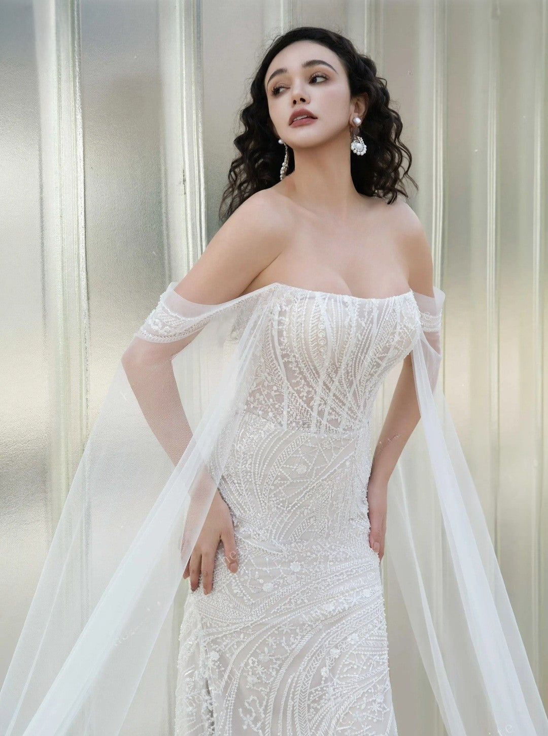 Woman wearing a white off-shoulder gown with intricate detailing against a neutral background