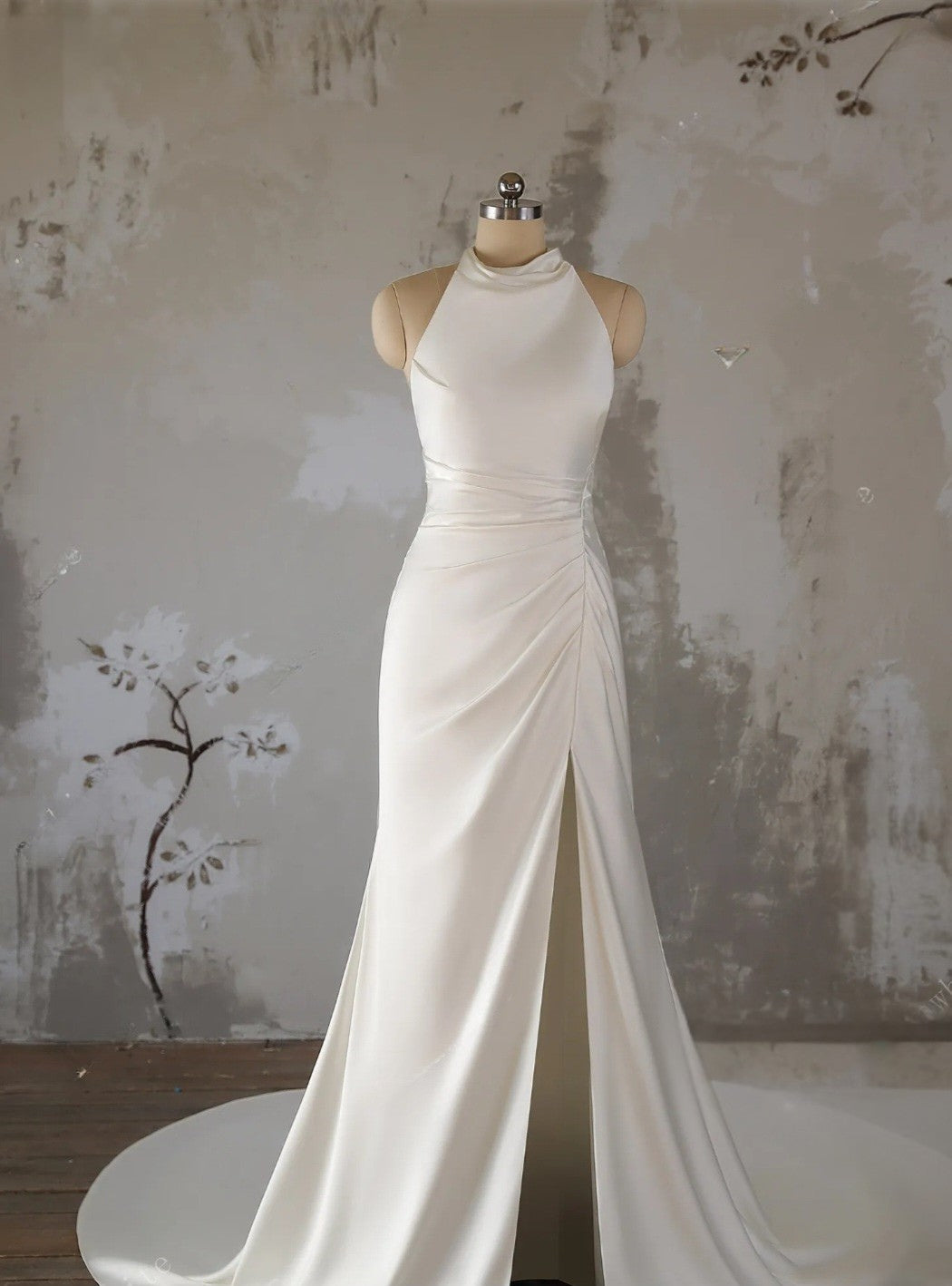 White evening gown on a mannequin against a textured wall.
