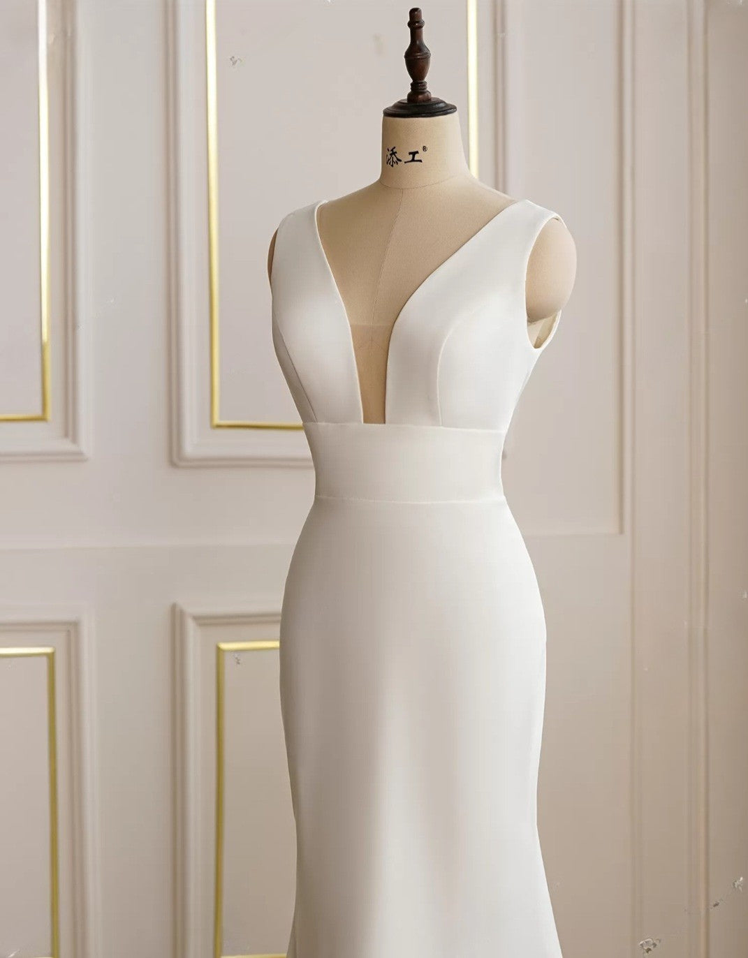 White evening gown on a mannequin against a white wall with gold trim