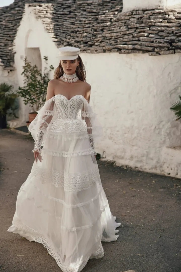 Woman in a white lace wedding dress standing in front of a stone building.