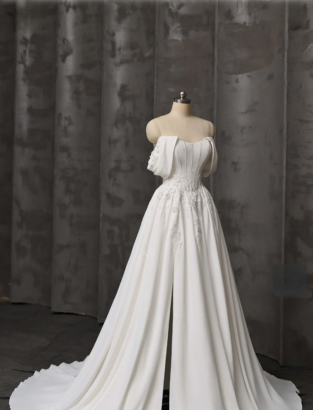 White wedding dress on a mannequin against a textured gray curtain background