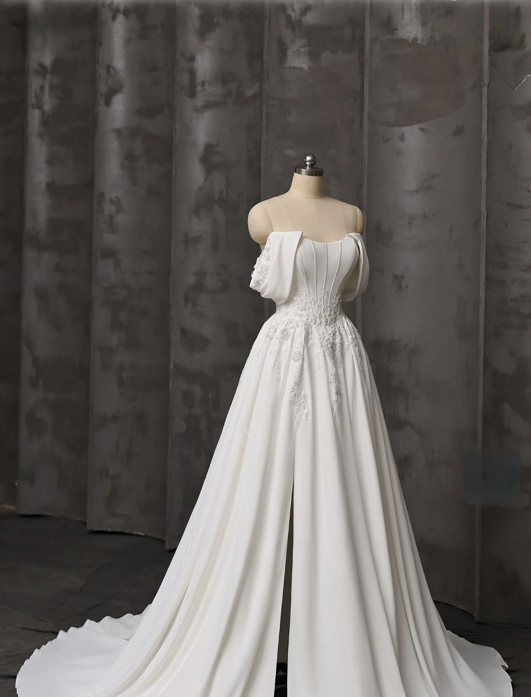 White wedding dress on a mannequin against a textured gray curtain background