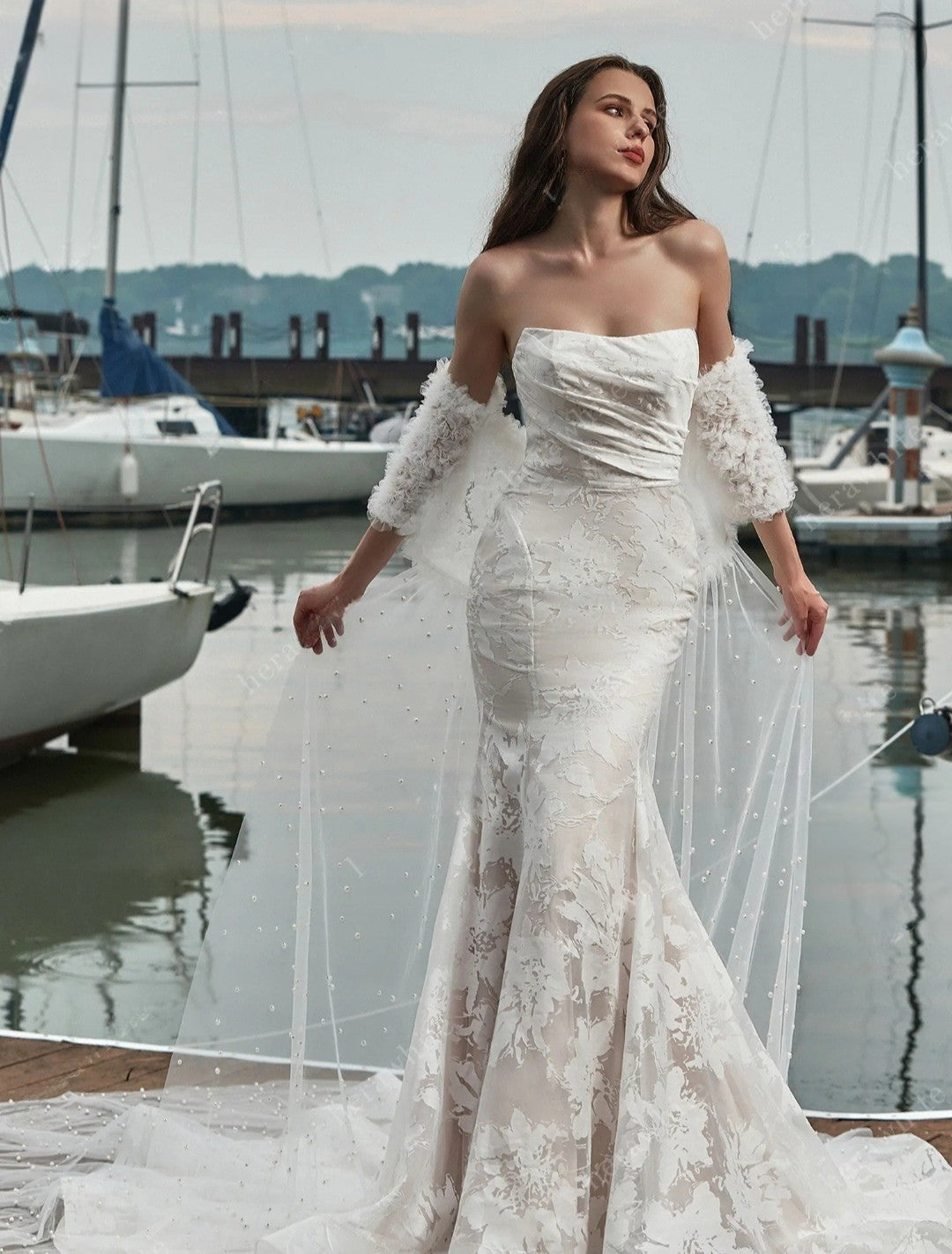 Woman in a white lace wedding dress standing by a marina with boats in the background