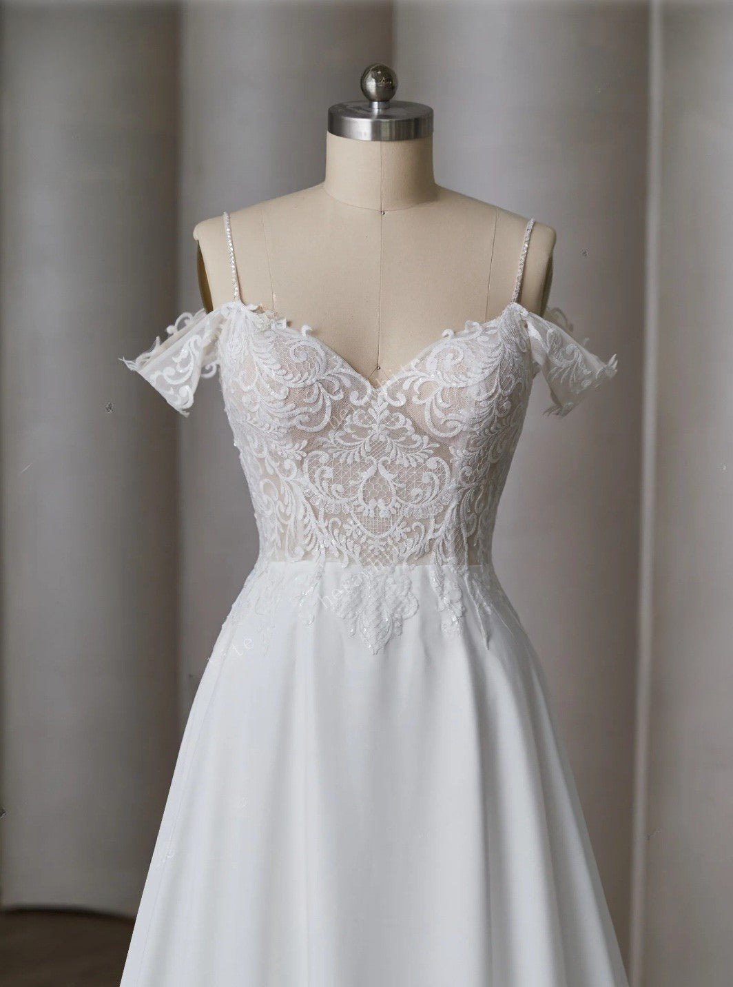White lace wedding dress on a mannequin against a neutral background