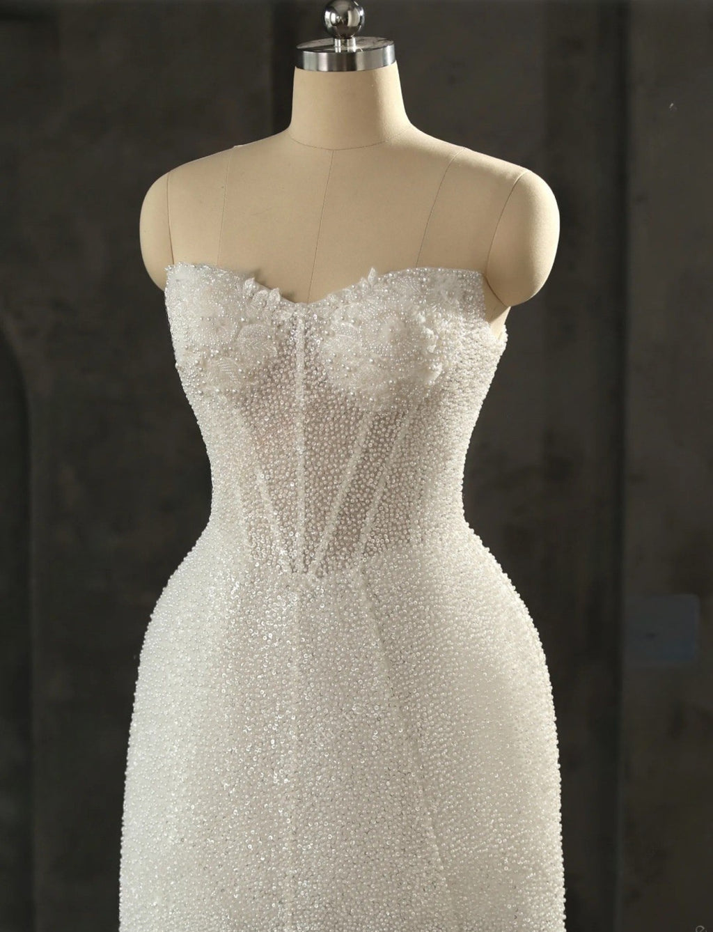 White beaded dress on a mannequin against a dark background