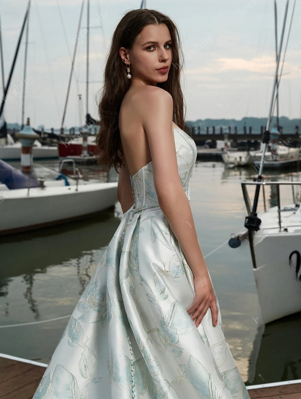 Woman in a light blue dress standing by a marina with boats in the background