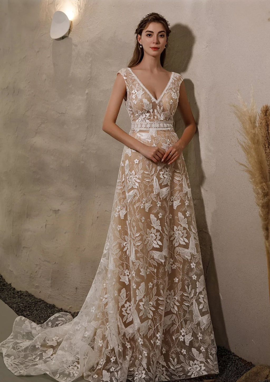 Woman wearing a lace evening gown against a neutral wall.