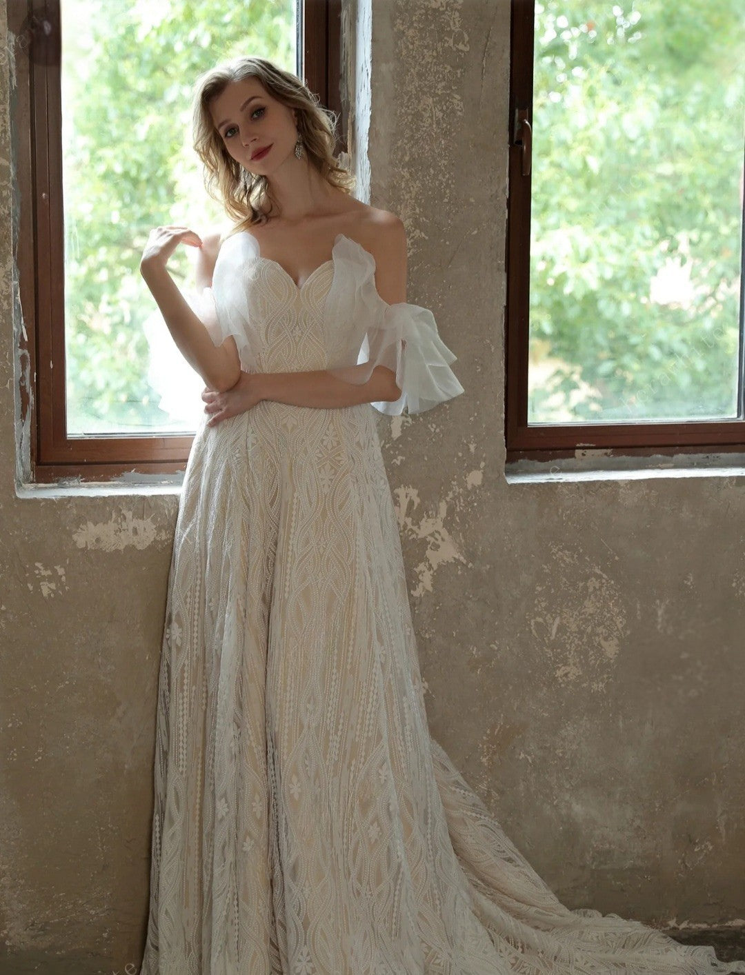 Woman in a white lace dress standing in front of a window with a textured wall.