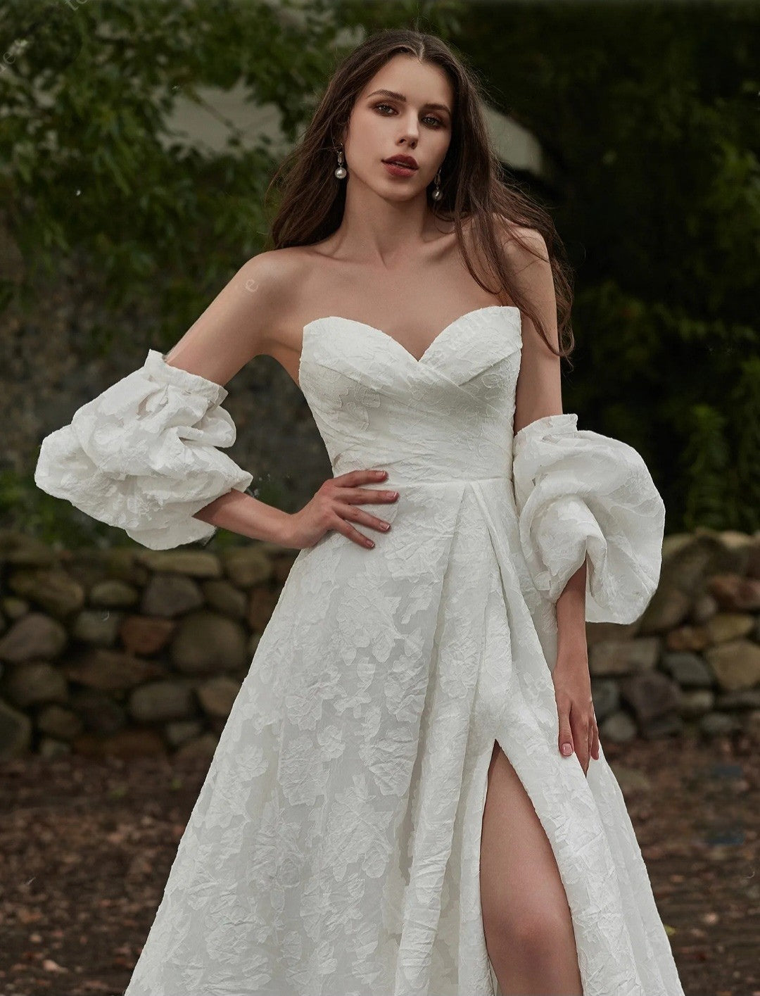 Woman in a white wedding dress with puffed sleeves standing outdoors.