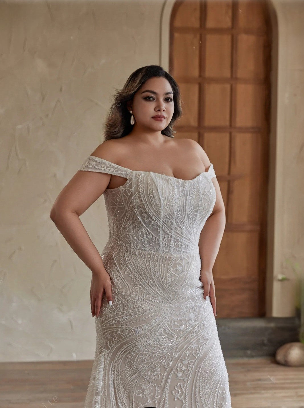 Woman wearing a white off-shoulder dress with intricate patterns in a neutral setting.