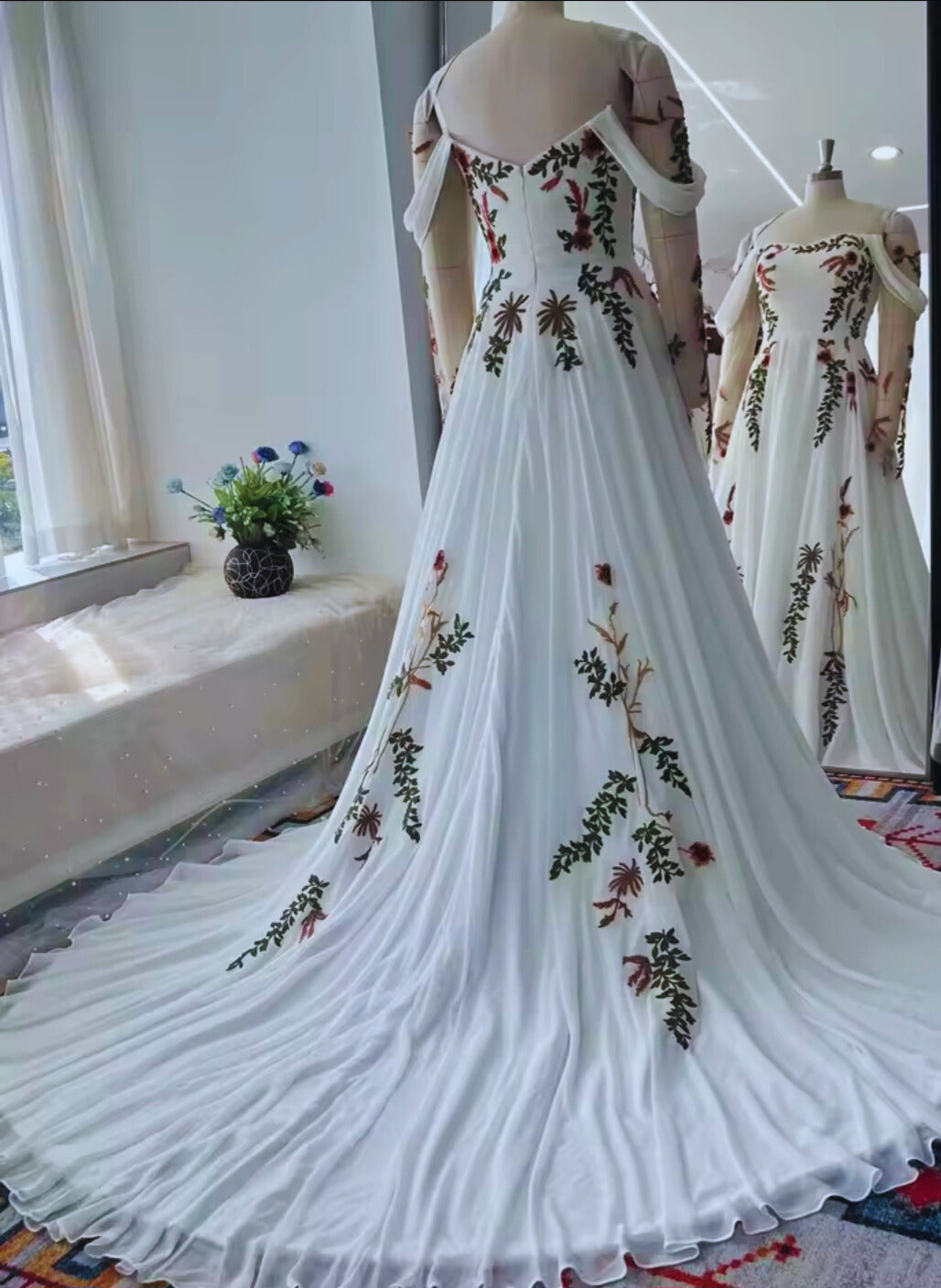 White evening gown with floral embroidery on a mannequin in a room.