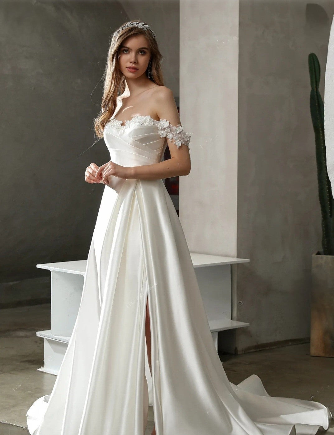Woman in a white wedding dress with floral details standing against a neutral background