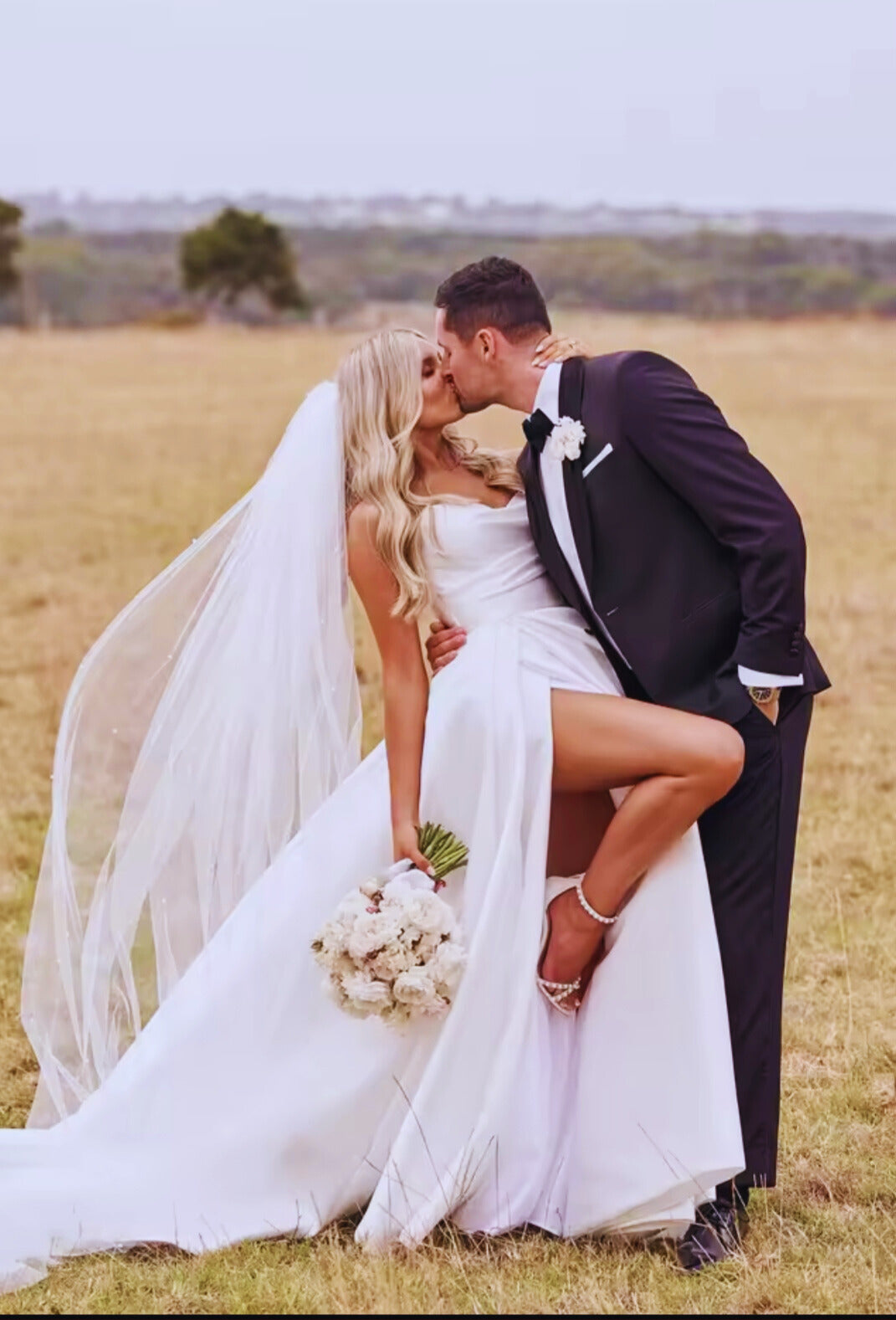 Couple in wedding attire kissing in a field