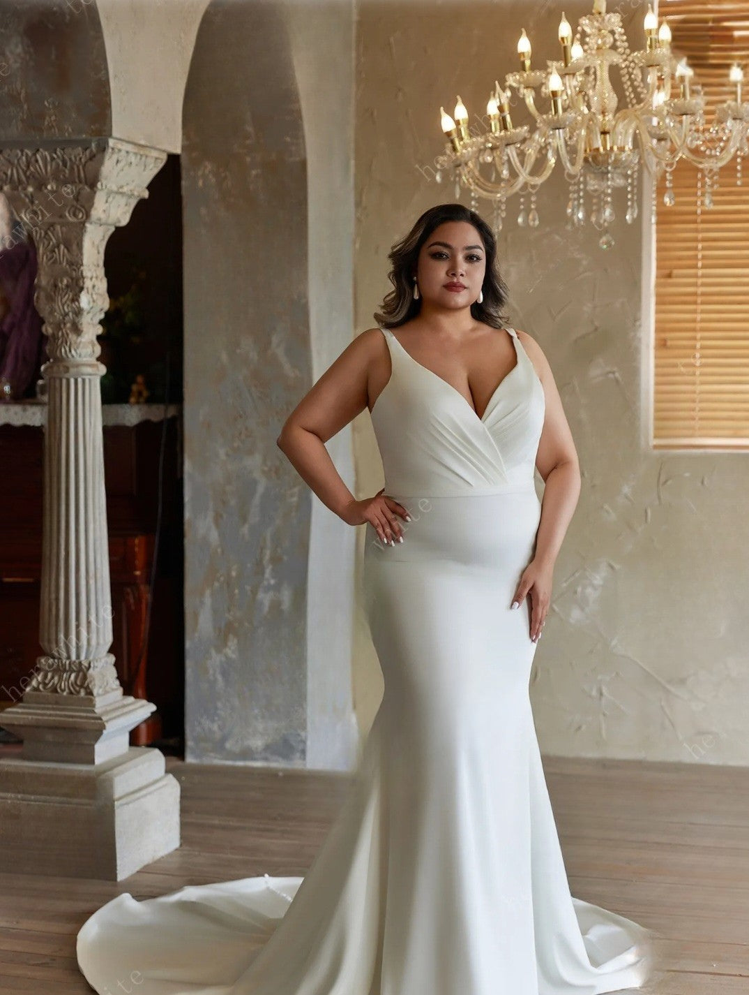 Woman in a white wedding dress standing in a elegant room with a chandelier.