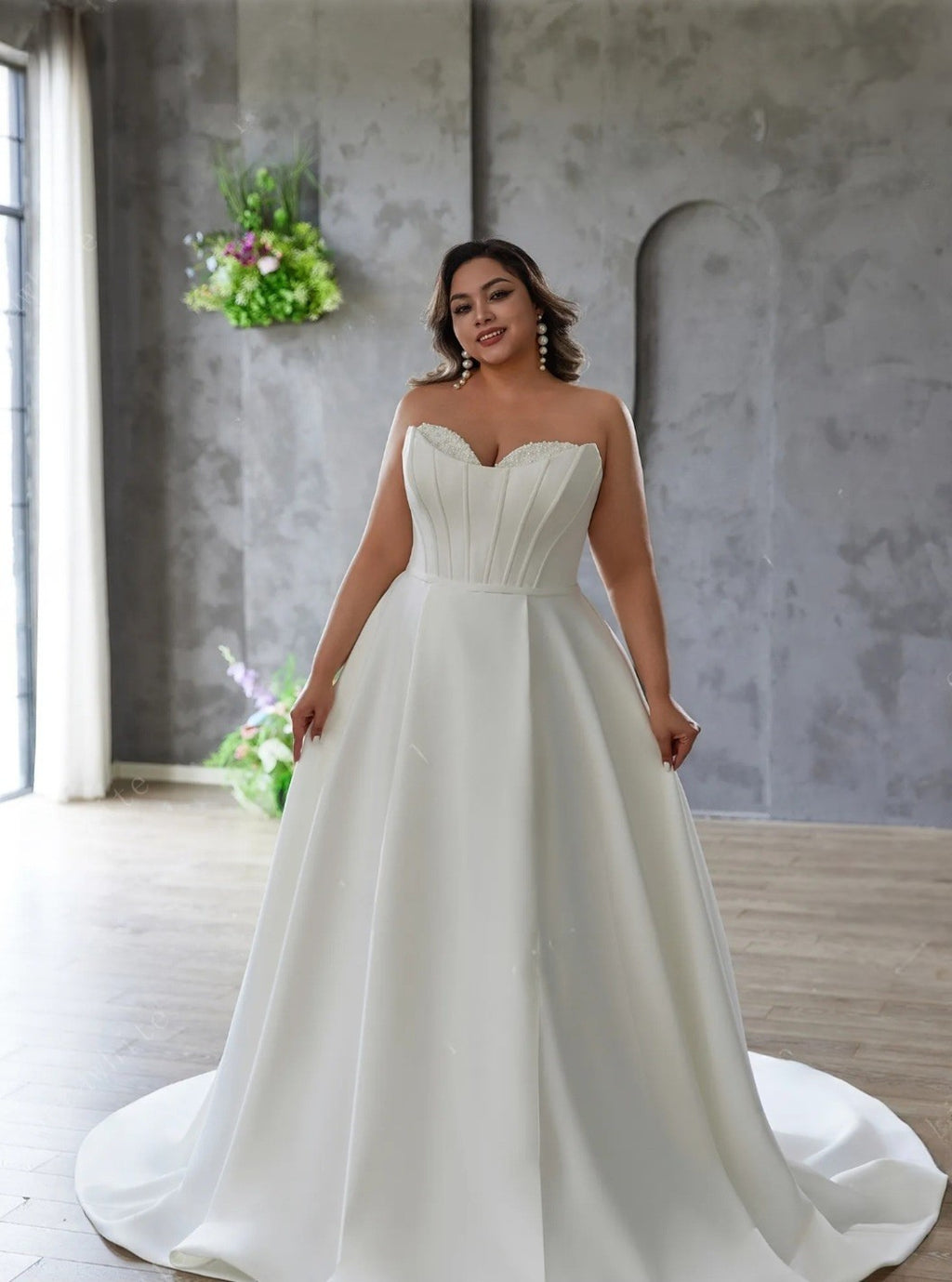 Woman wearing a white strapless gown in a room with a gray wall and plants.