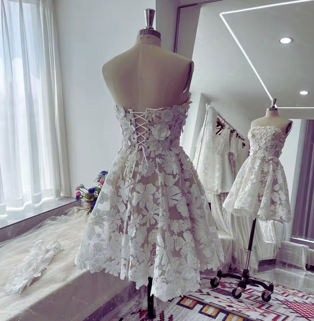 White lace dress on a mannequin in a room with mirrors and other dresses.
