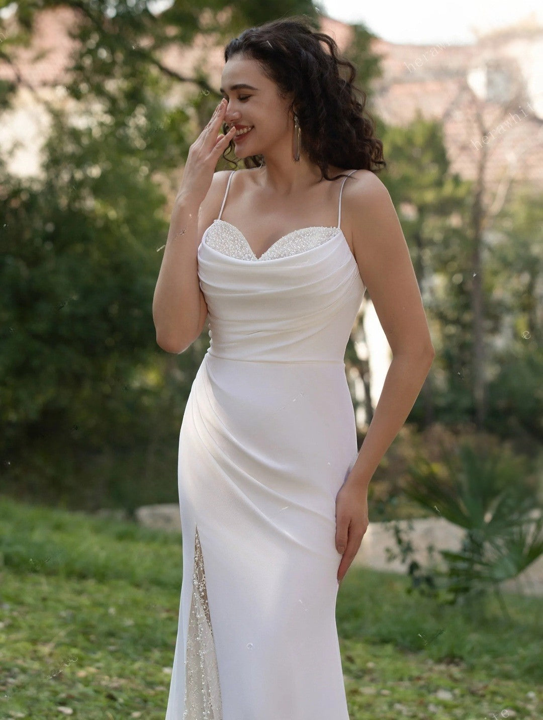 Woman in a white wedding dress standing outdoors with greenery in the background