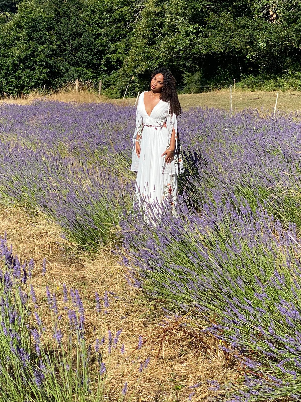 Woman in a white dress standing in a lavender field with green trees in the background