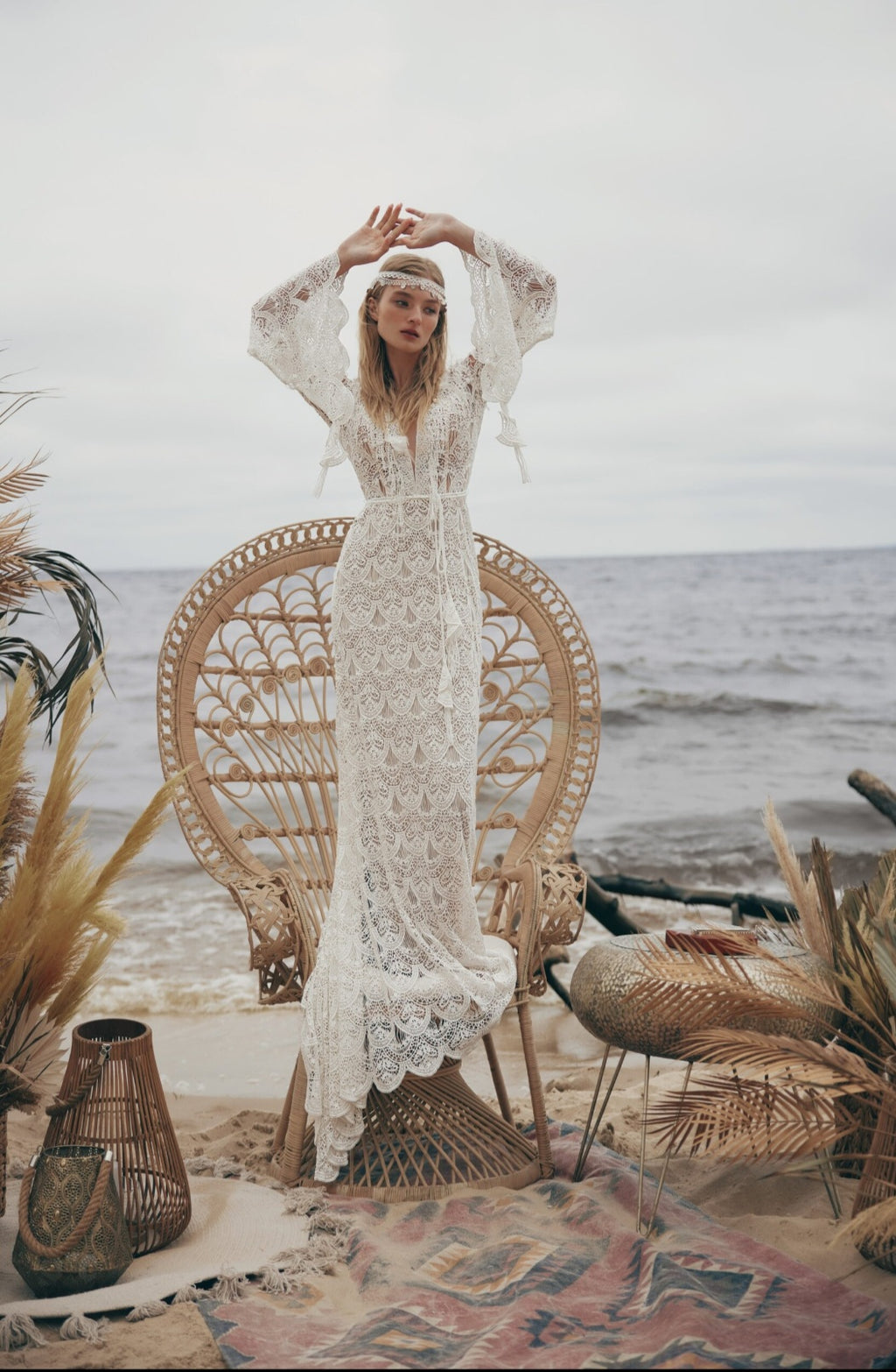 Woman in a white lace dress sitting on a wicker chair by the beach.