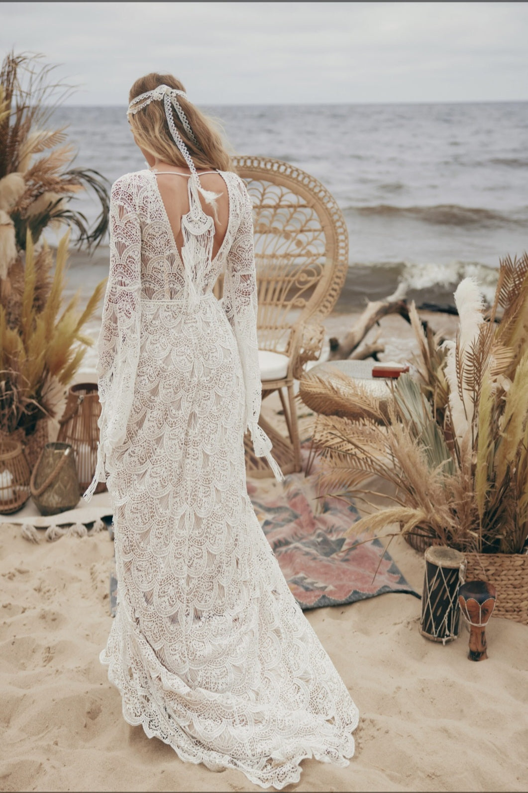 Woman in a lace dress standing on a beach with decorative elements.