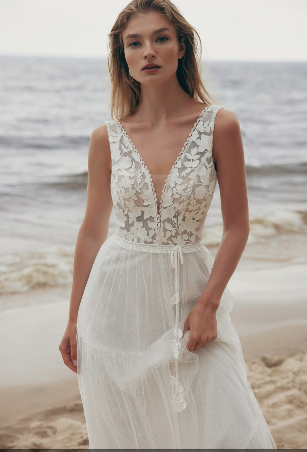 Woman in a lace dress standing on a beach with ocean in the background