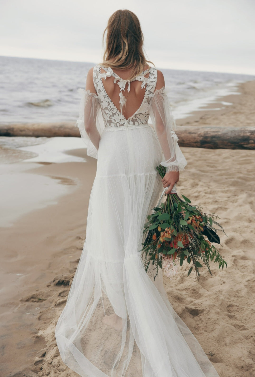 Woman in a white wedding dress holding a bouquet on a beach