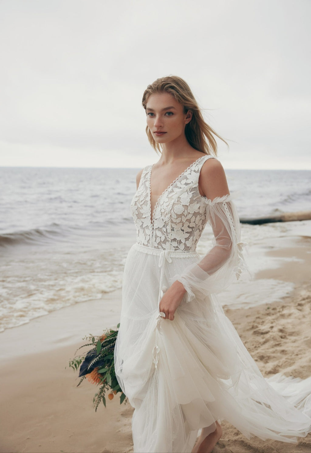 Woman in a white wedding dress standing on a beach with ocean in the background