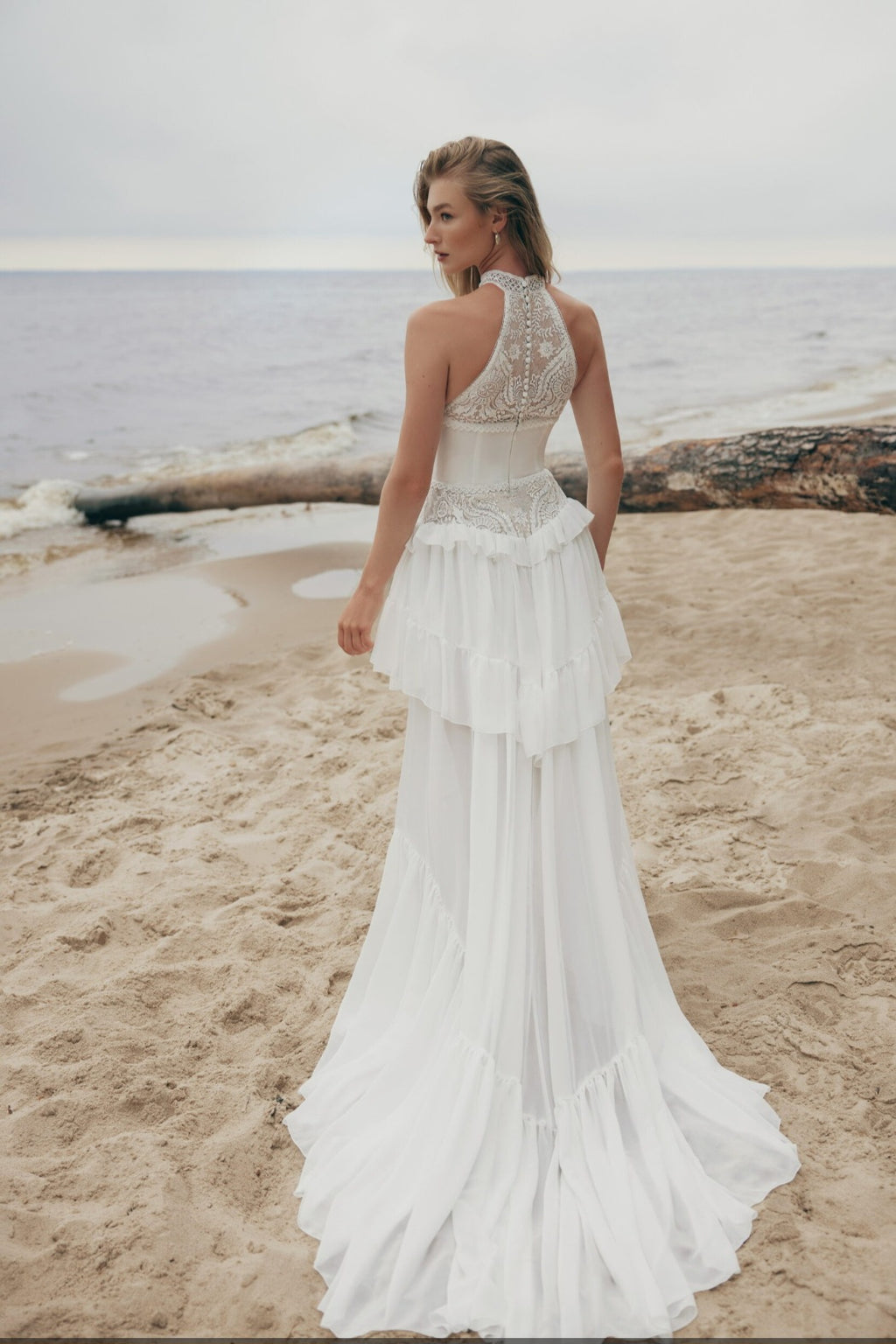 Woman in a white wedding dress standing on a beach with ocean in the background