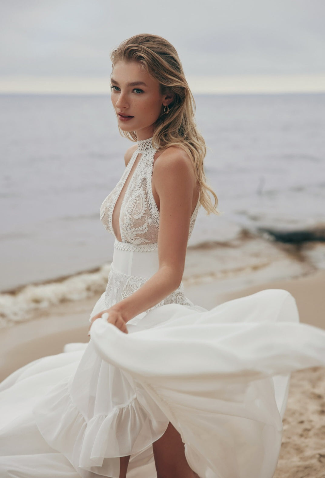 Woman in a white lace dress standing on a beach with ocean in the background
