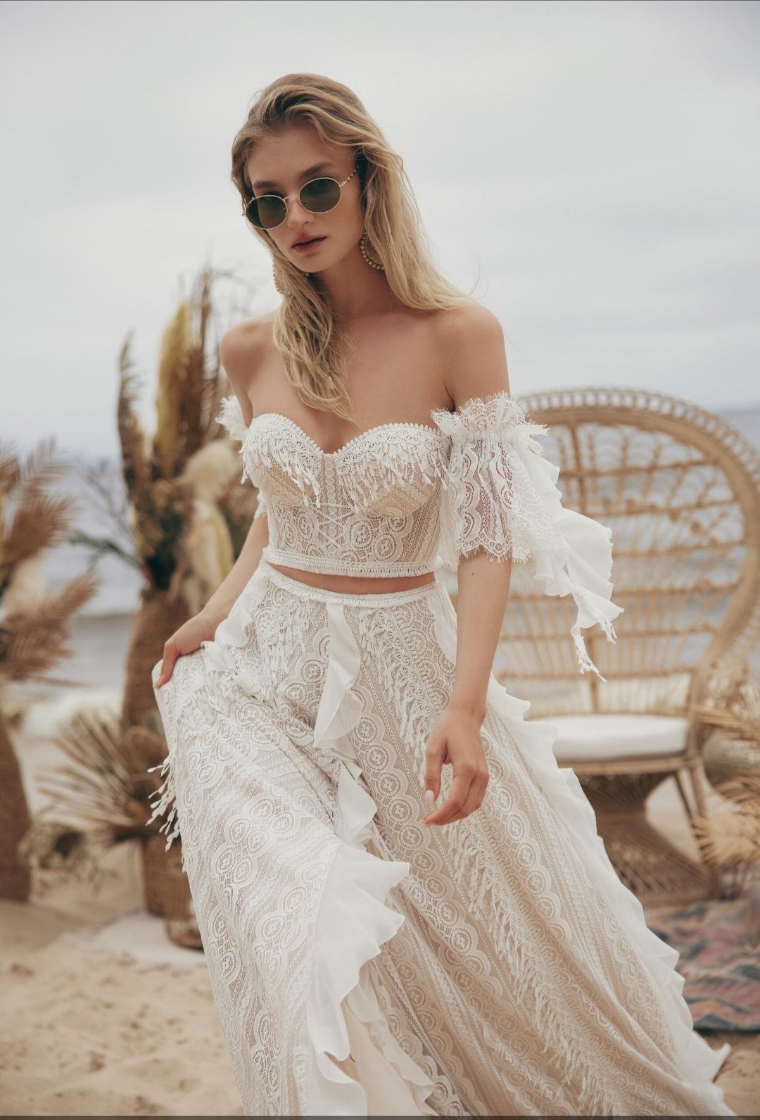 Woman in a white lace outfit standing in a desert-like setting with cacti and a chair.