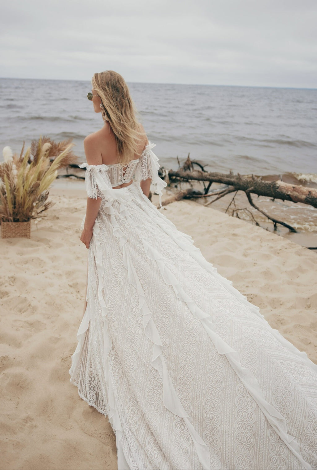 Woman in a white off-shoulder dress standing on a beach with ocean view