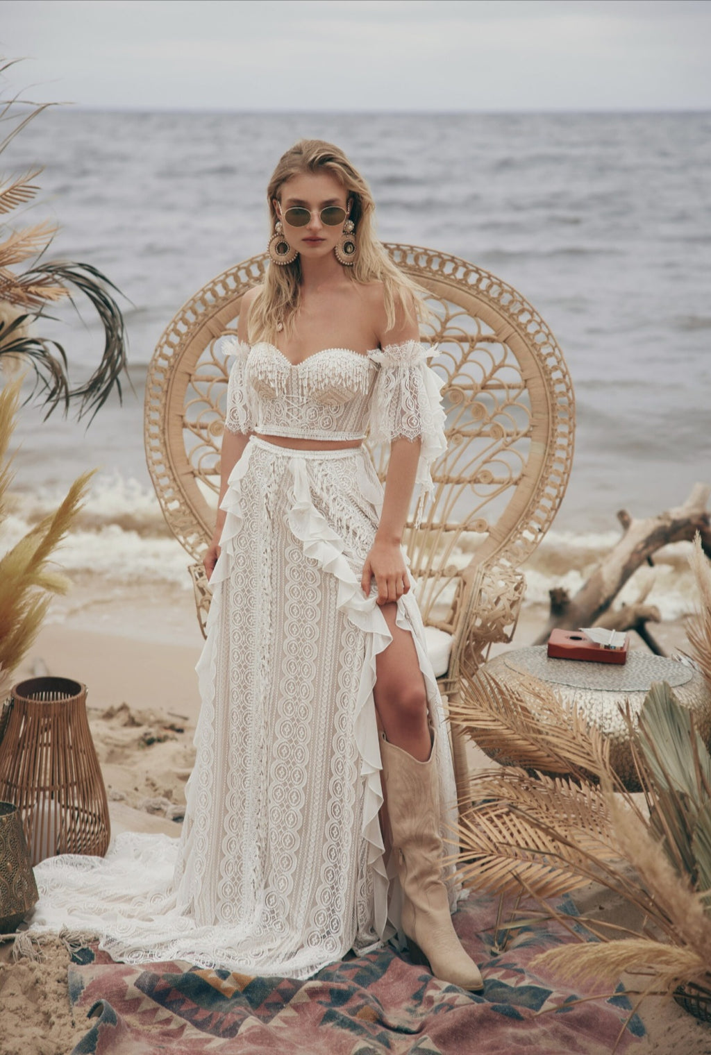 Woman in a white lace dress with a high slit standing on a beach with ocean view.