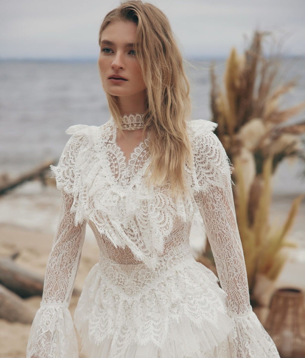 Woman wearing a lace dress on a beach with ocean and plants in the background