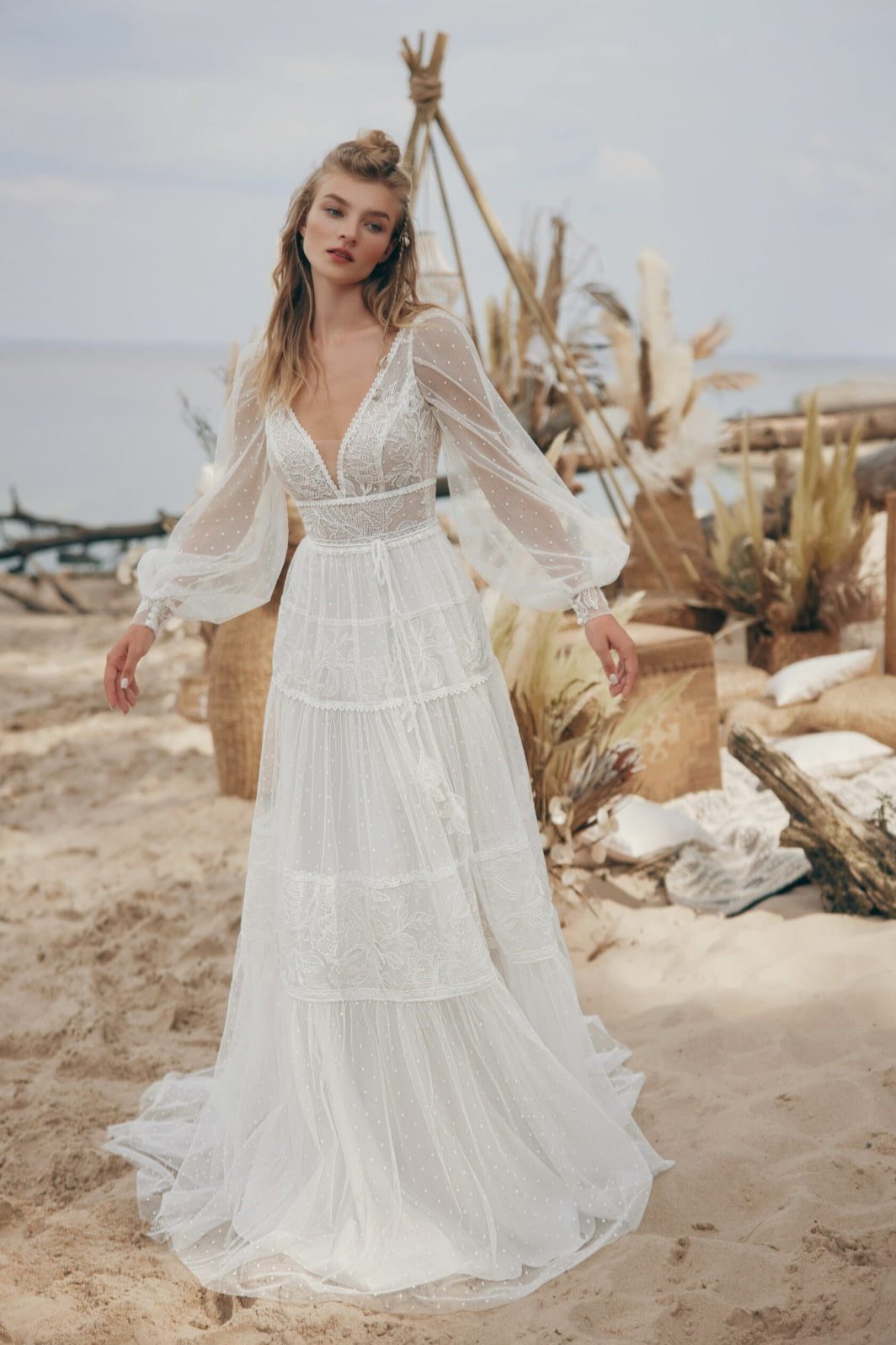 Woman in a white dress standing on a beach with driftwood and plants in the background
