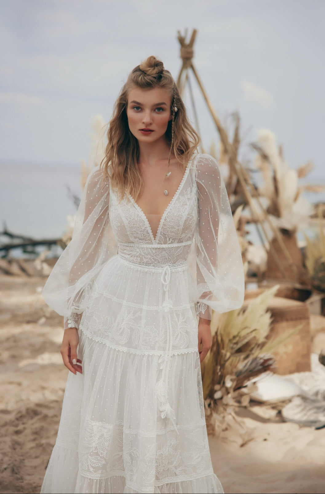 Woman in a white dress standing in a desert-like setting with desert plants and a tent in the background.
