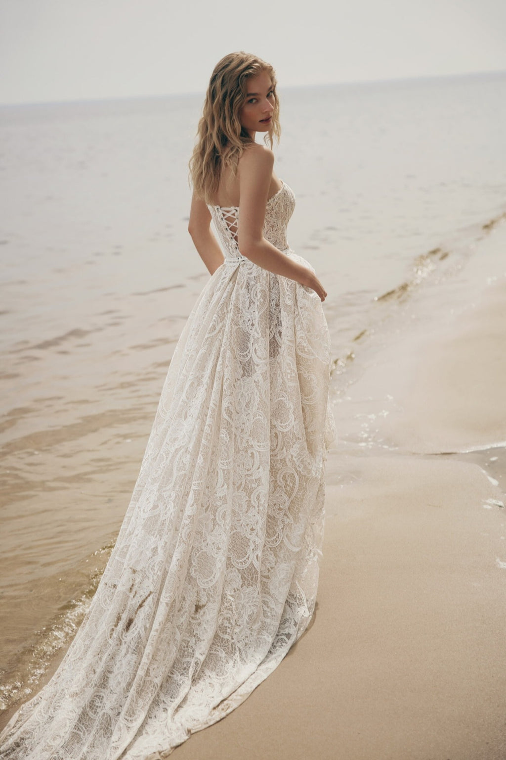 Woman in a lace wedding dress standing on a beach
