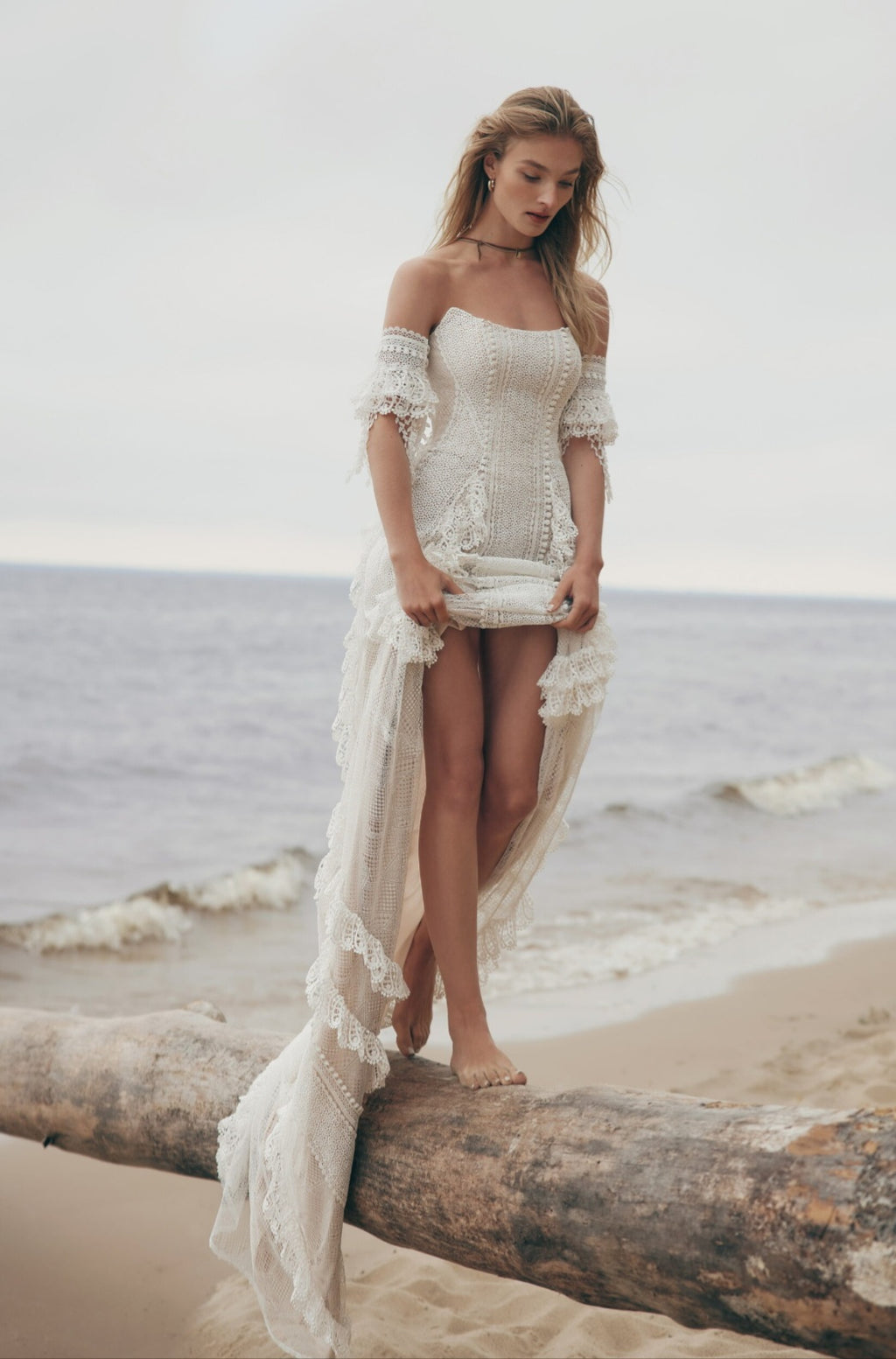 Woman in a white lace dress standing on a beach with ocean in the background