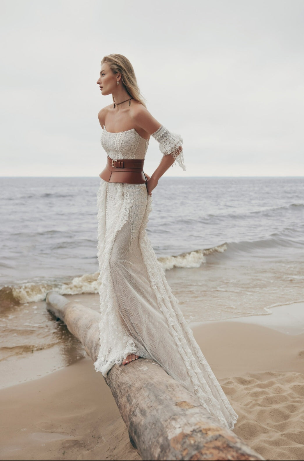 Woman in a white lace dress standing on a beach with ocean waves in the background