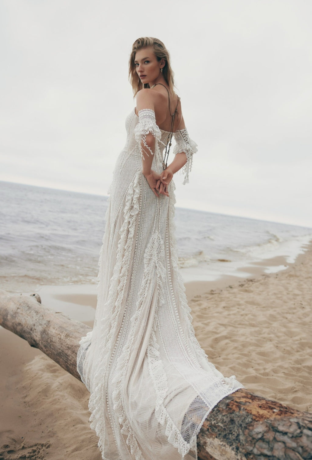 Woman in a white lace dress standing on a beach with ocean in the background