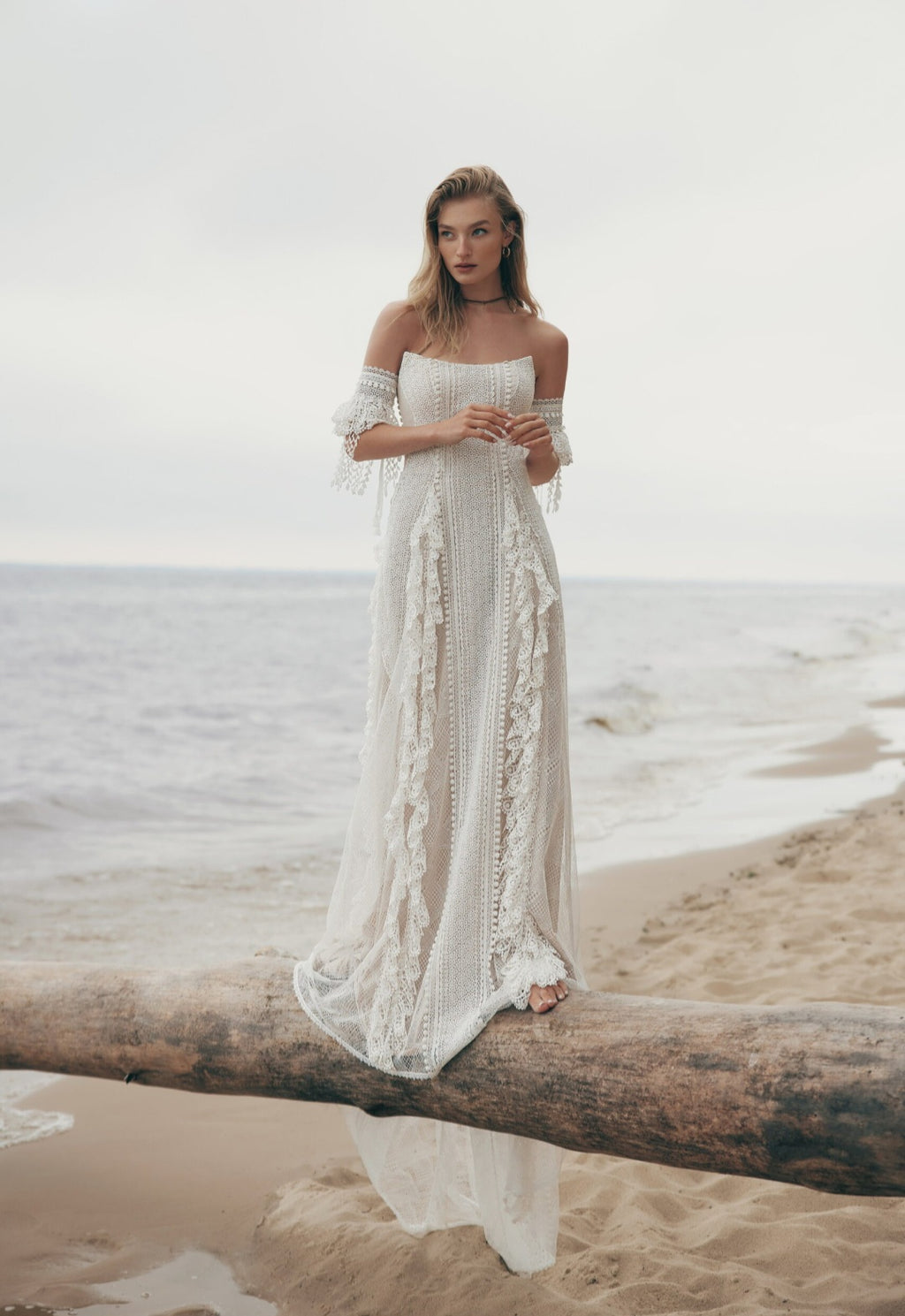 Woman in a white lace dress standing on a beach with ocean waves in the background
