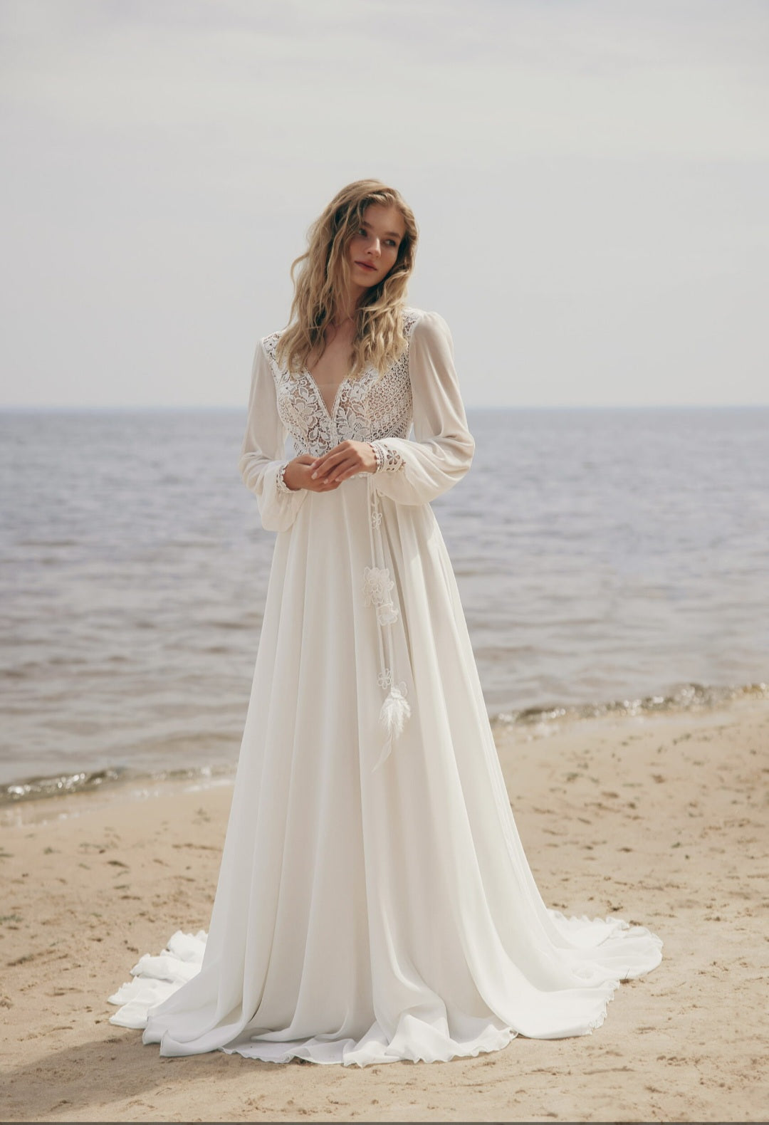 Woman in a white lace dress standing on a beach with ocean in the background