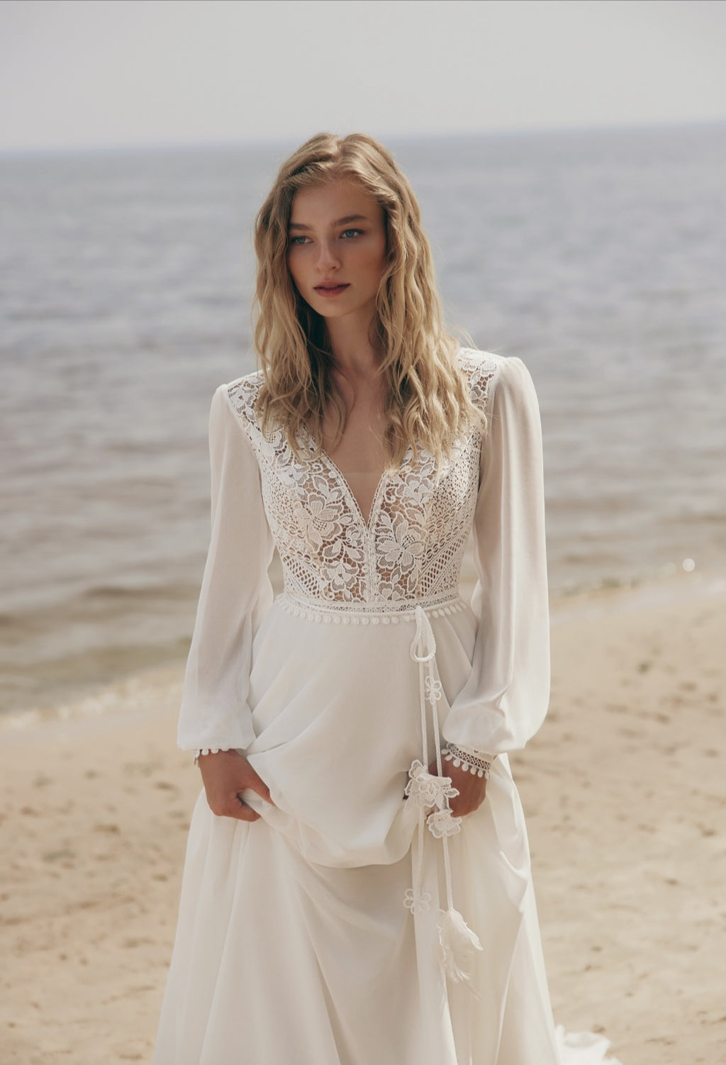 Woman in a white lace dress standing on a beach with ocean in the background