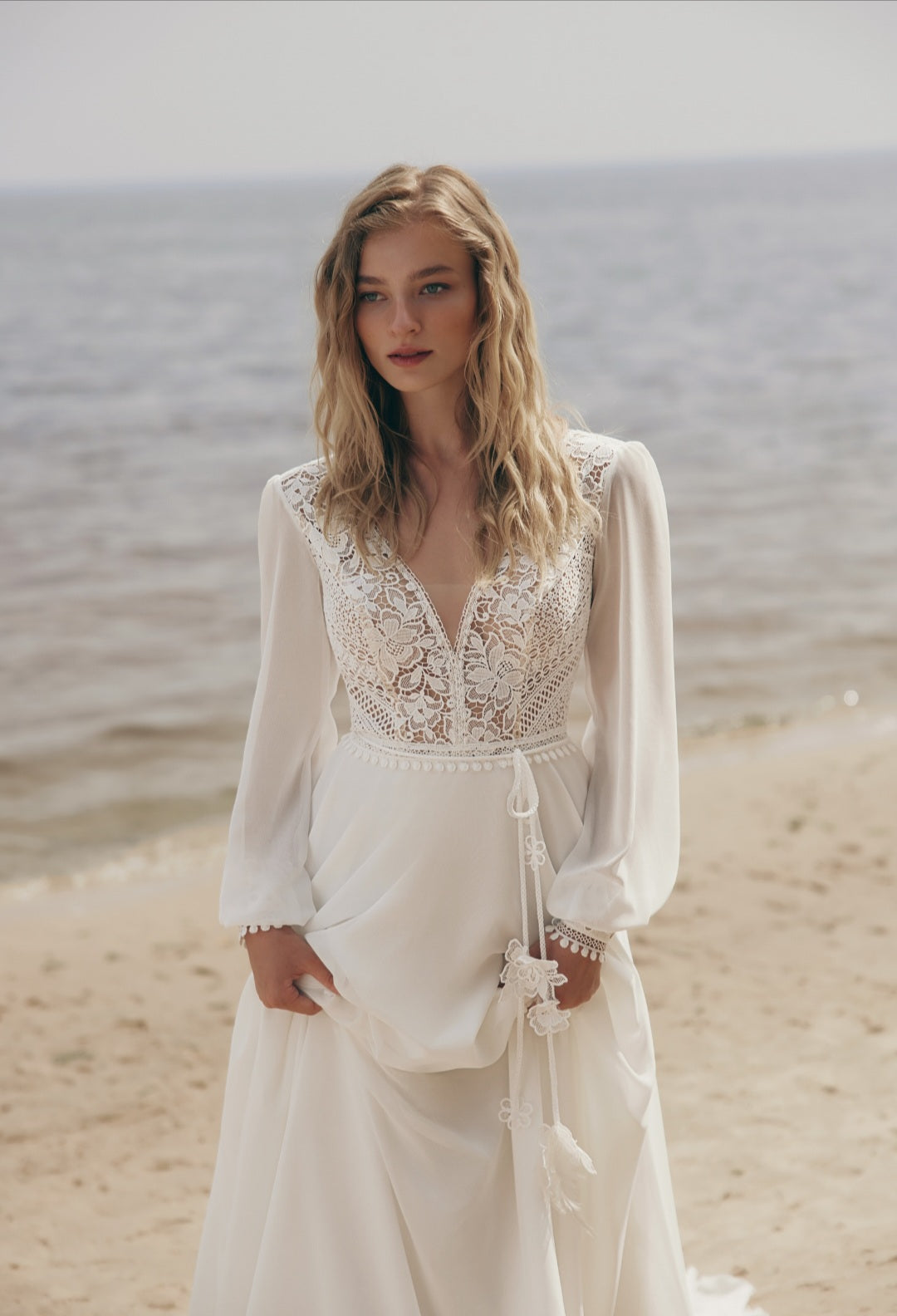 Woman in a white lace dress standing on a beach with ocean in the background