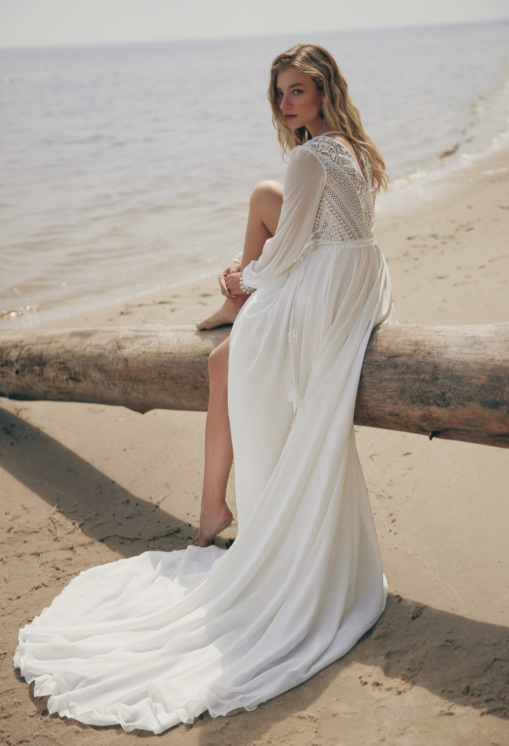 Woman in a white dress sitting on a log by the beach