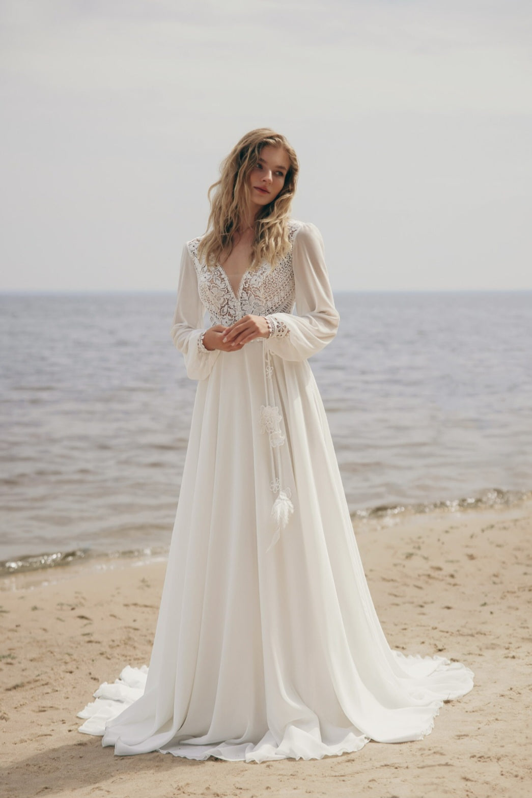 Woman in a white lace dress standing on a beach with ocean in the background